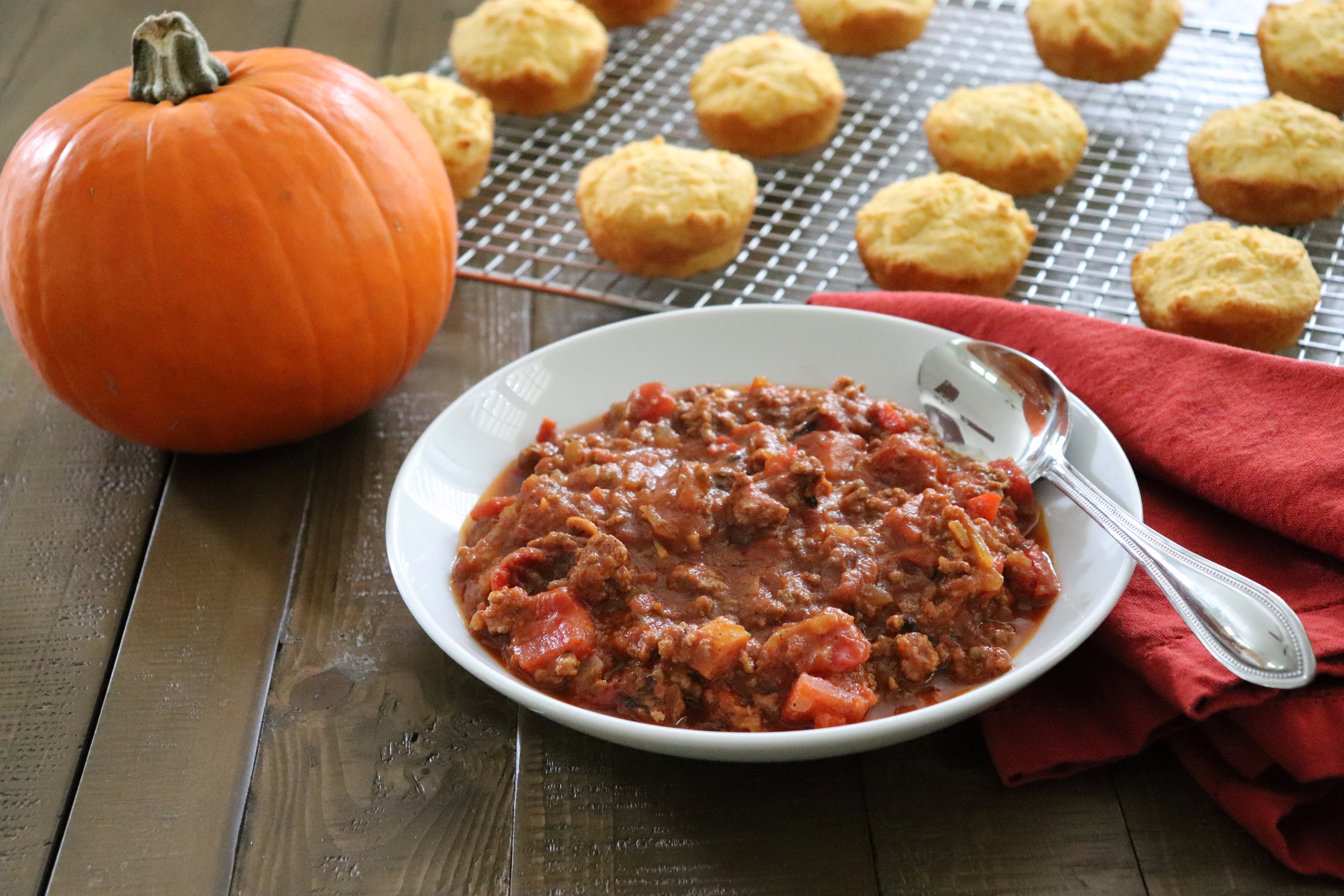 Bowl of Pumpkin Chili with cornbread muffins and a small pumpkin in the background