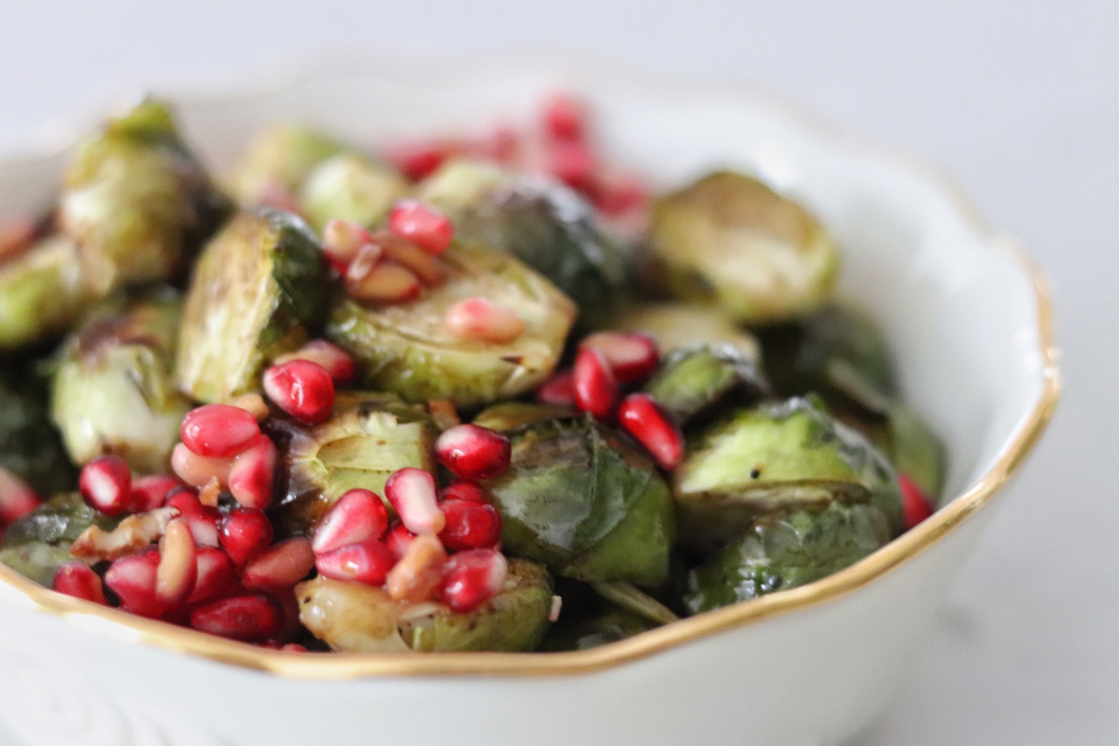Roasted Brussels Sprouts with Balsamic and Pomegranate Seeds in a white bowl with a gold rim