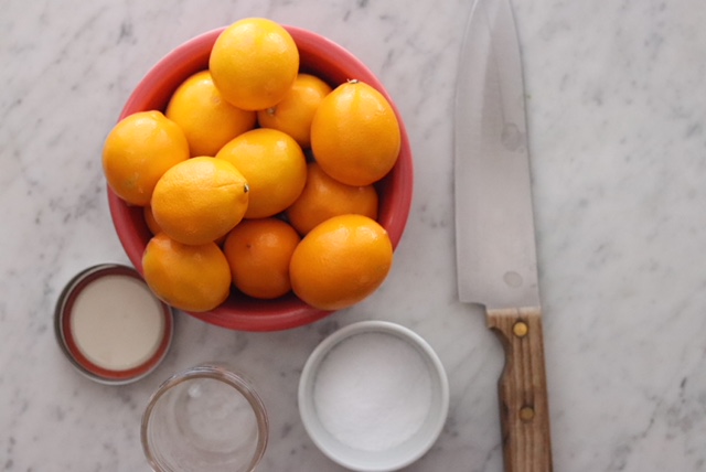 Bowl of Meyer lemons, kosher salt, knife, cutting board, and jar for making Preserved Lemons