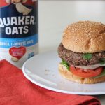 Oat Black Bean Vegetable Burger on a bun with a carton of Quaker Oats in the background