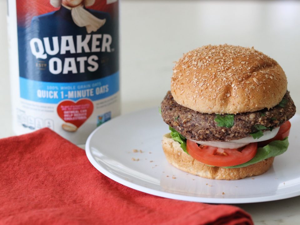 Oat Black Bean Vegetable Burger on a bun with a carton of Quaker Oats in the background