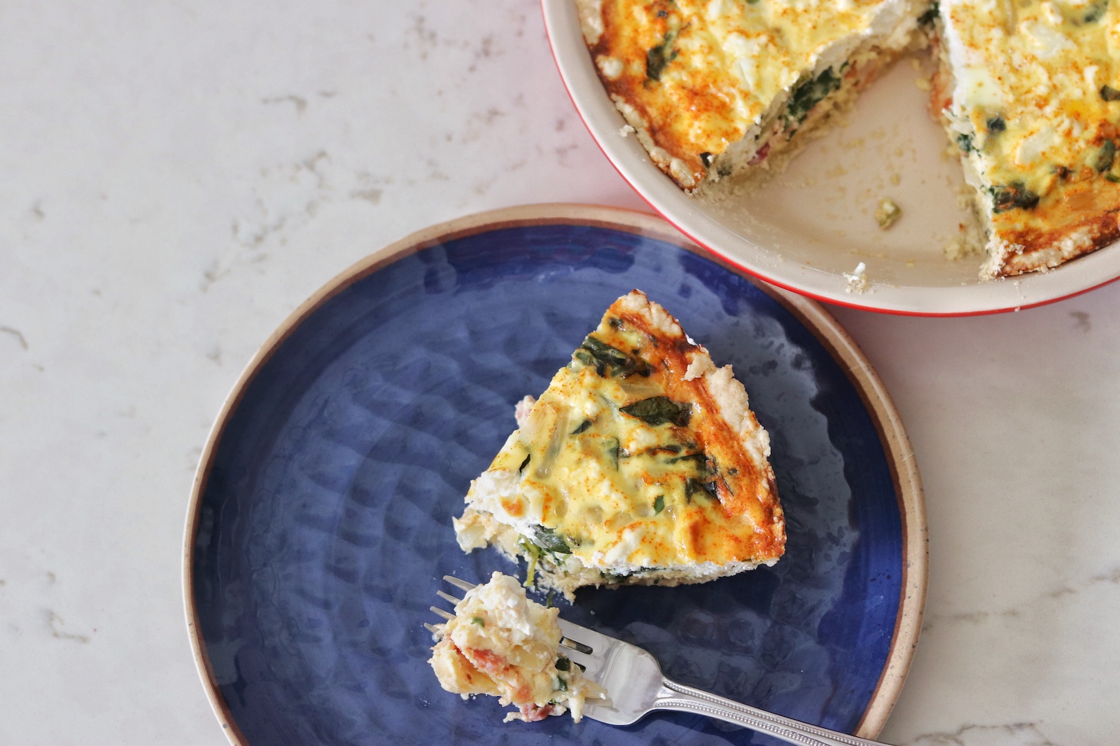 Pie plate with Bacon, Spinach and Sweet Onion Quiche and a plate with one slice and a bite taken out
