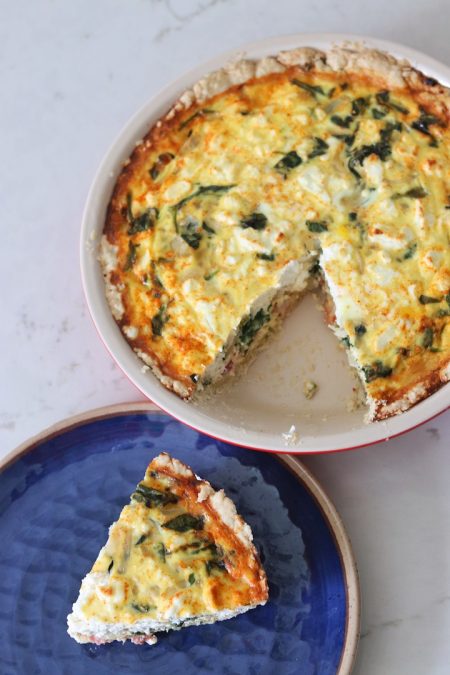 Pie plate with Bacon, Spinach and Sweet Onion Quiche and a slice of quiche on a blue plate