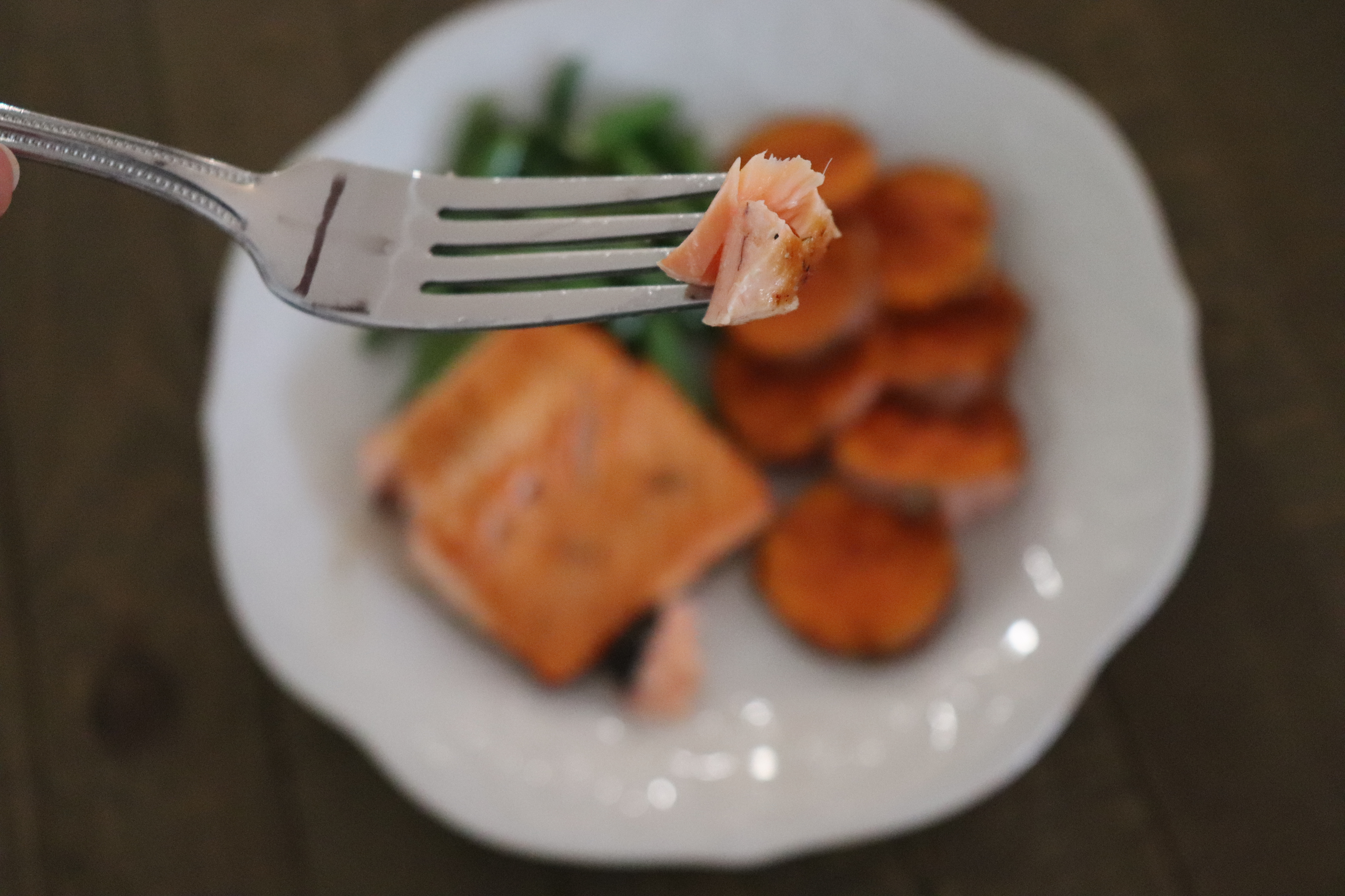 Bite of flaky salmon with a plate of salmon, sweet potatoes and green beans in the background